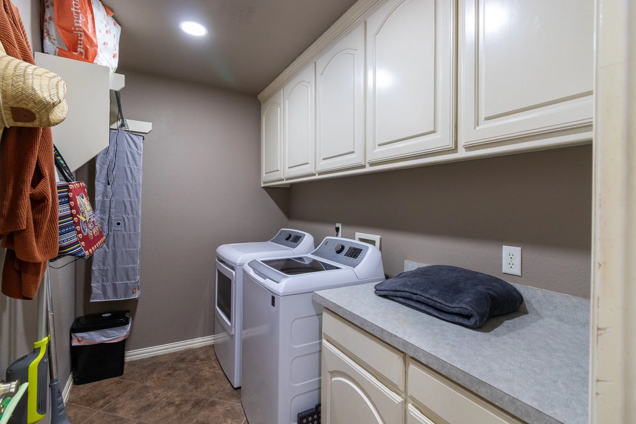 Laundry area featuring built-in upper cabinetry, a solid surface countertop, lower cabinetry, and tiled flooring