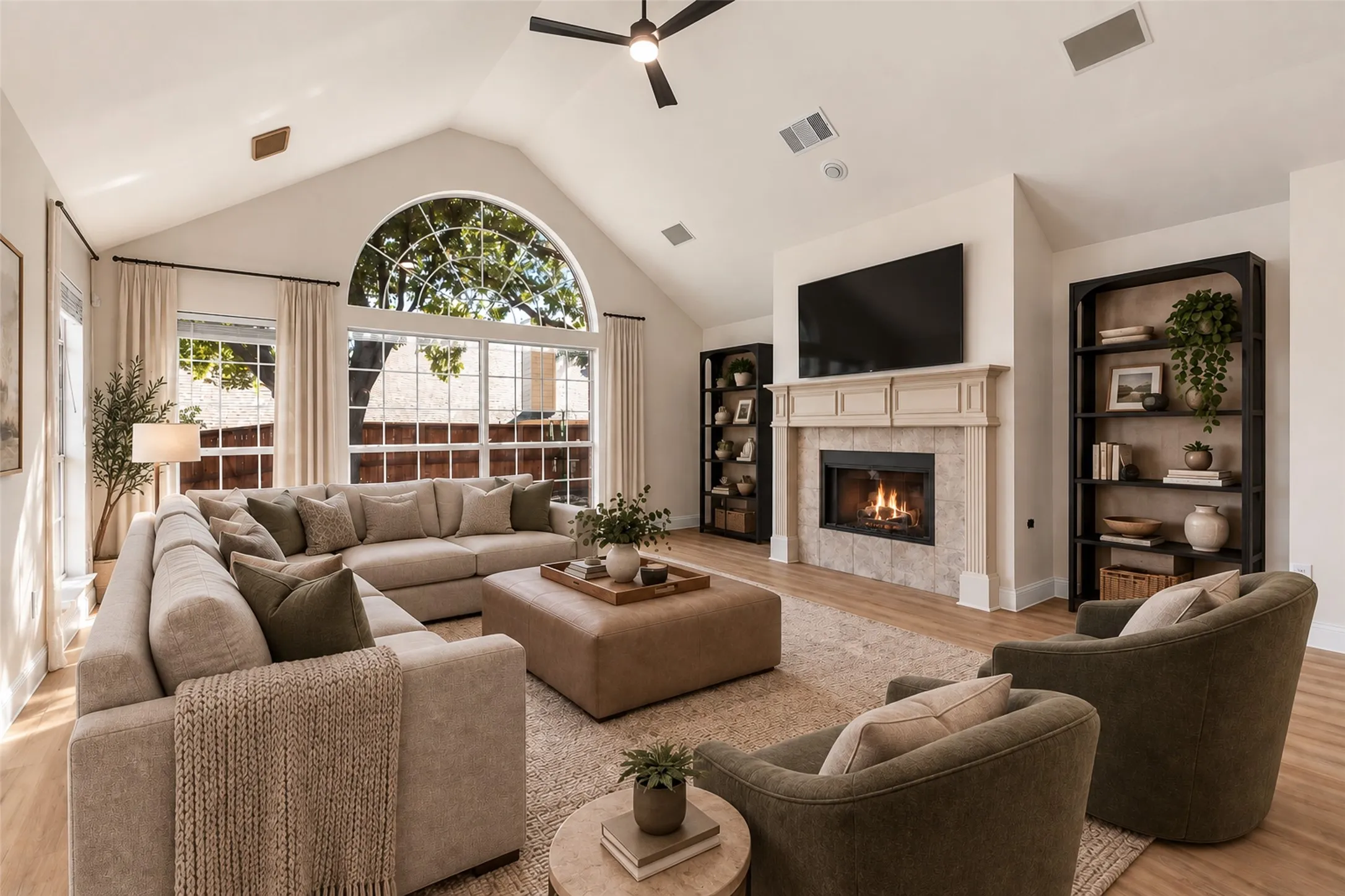 Virtually staged Vaulted ceiling with a ceiling fan, arched window, built-in shelving, fireplace with a tiled surround, and wood-finish flooring