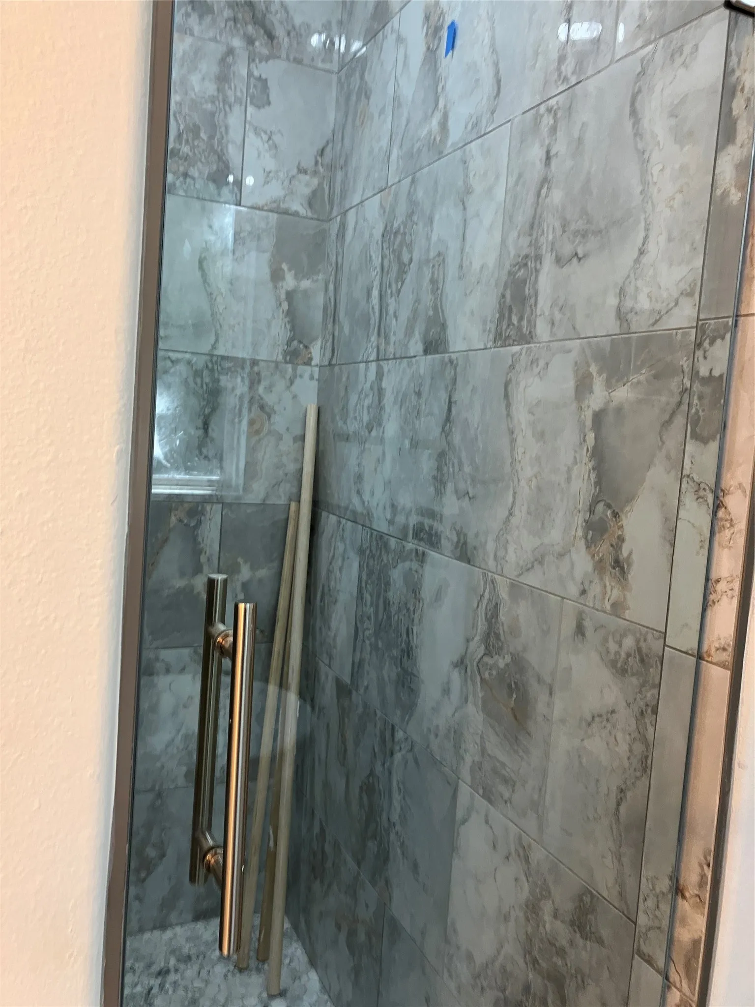 Glass-enclosed shower with large format tile walls, recessed shower niche, pebble-finish shower floor, and brushed metal hardware