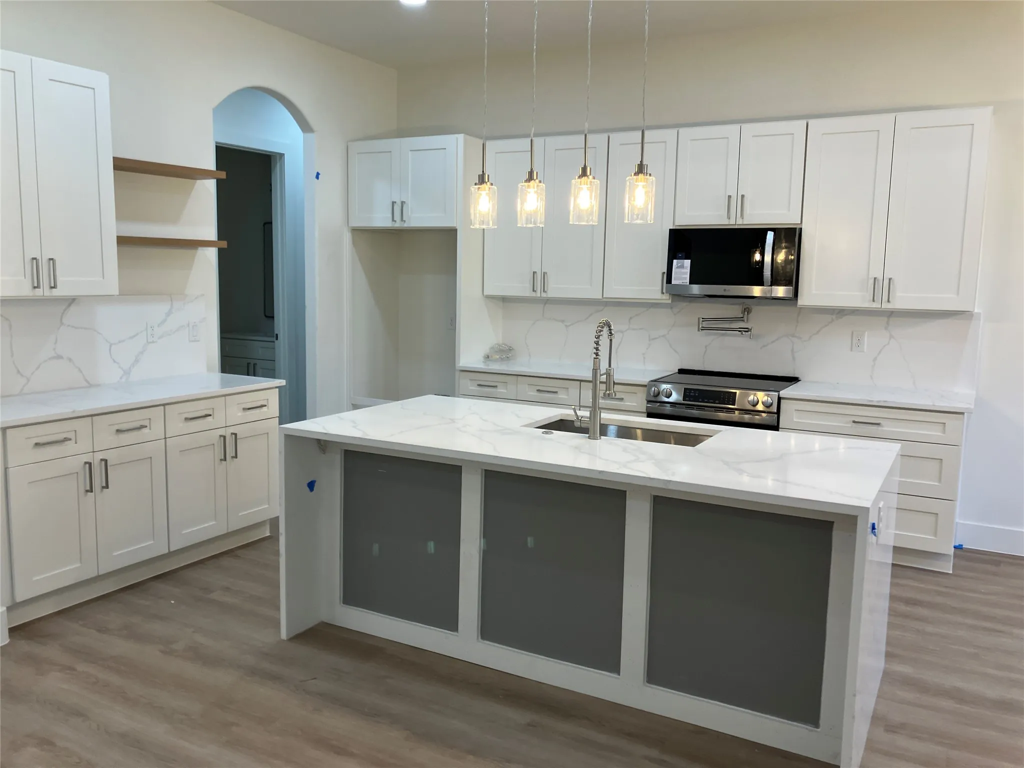 Kitchen featuring an island with a built-in sink, white shaker cabinetry, patterned solid surface countertops with matching backsplash, wood-finish flooring, and recessed lighting