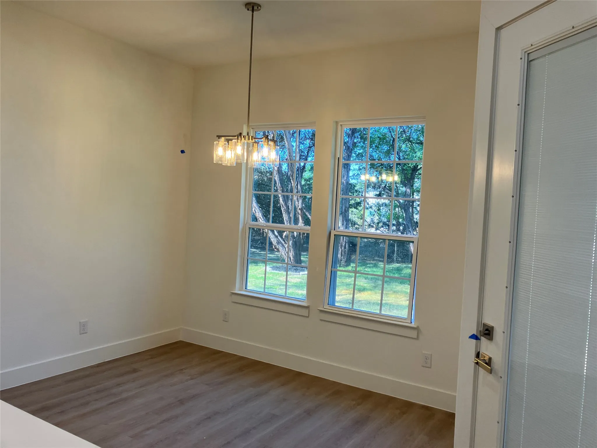 Wood-finish flooring, two large windows with exterior scenery, and a contemporary linear chandelier with clear glass shades