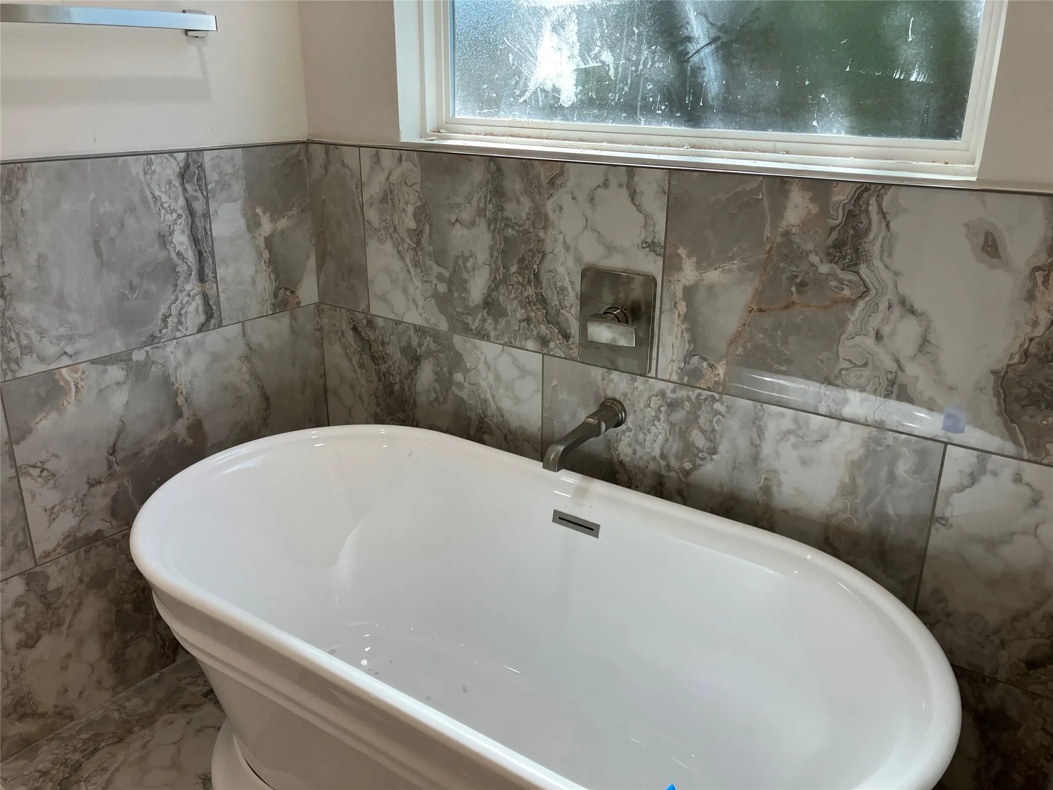 Freestanding soaking tub with a wall-mounted faucet, complemented by large-format gray and white tile surrounds