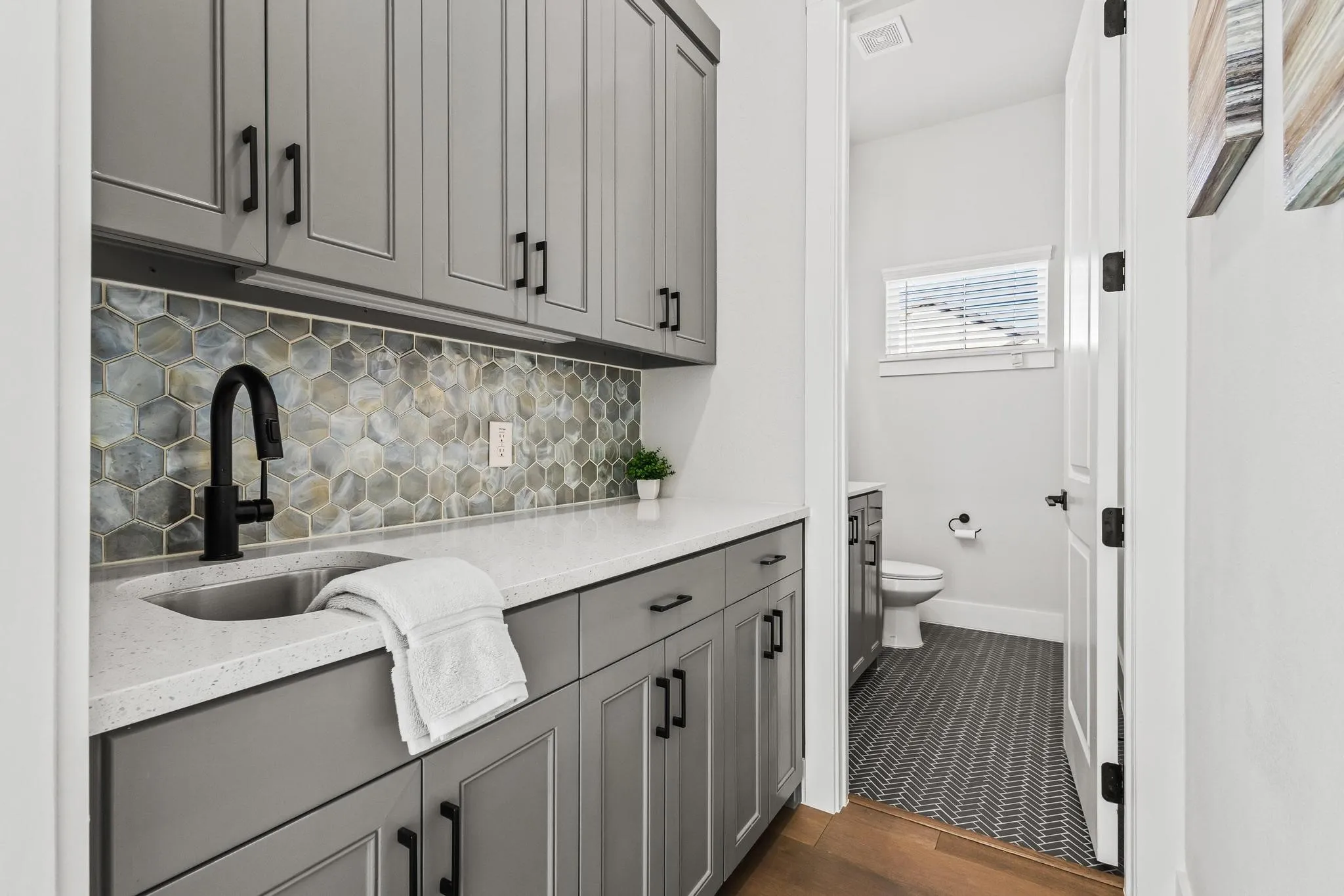 Bar with gray cabinets, decorative backsplash, light stone counters, and dark wood-type flooring leading to half bath