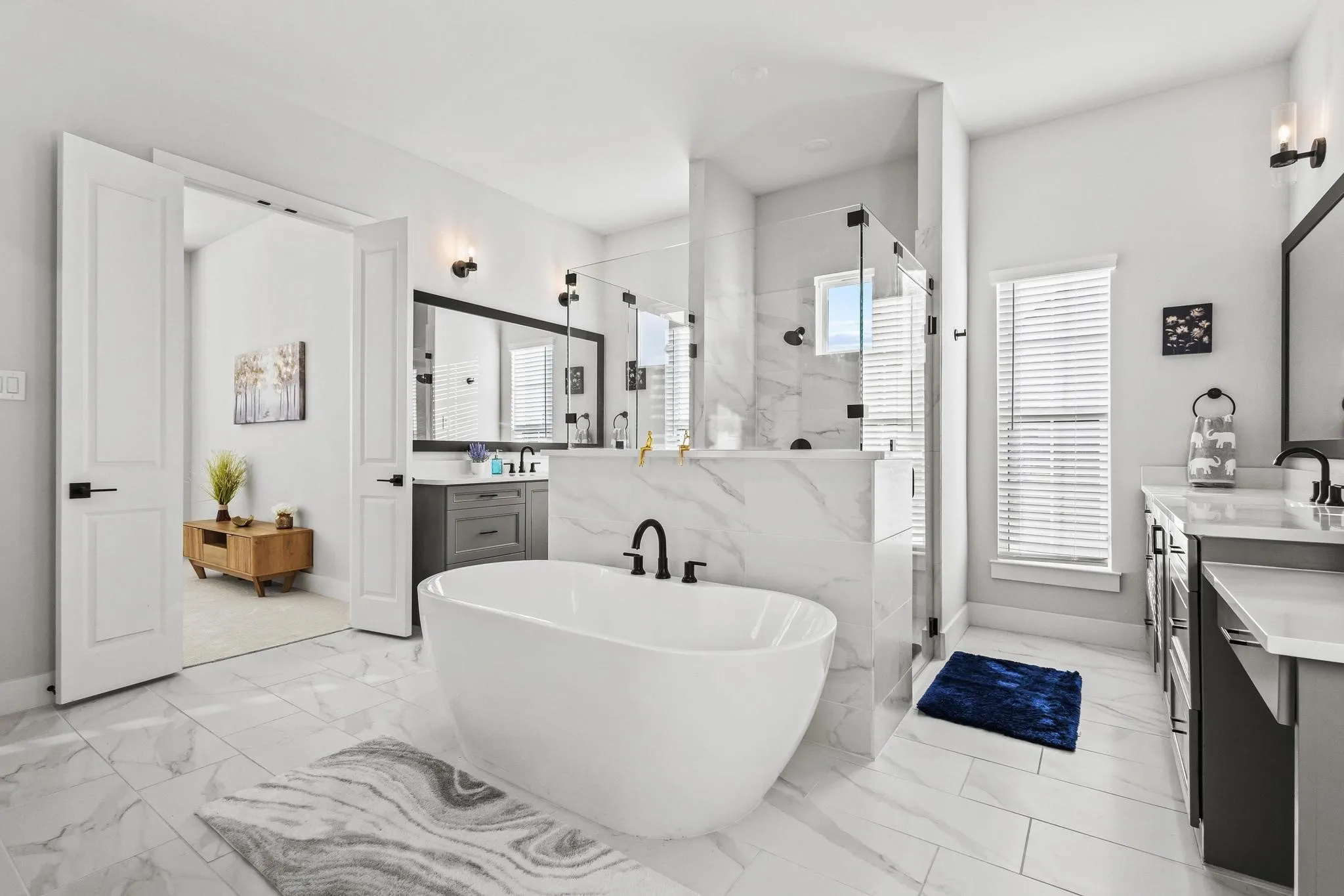 Bathroom featuring a freestanding bath, two vanities, a marble finish shower, and light marble finish flooring