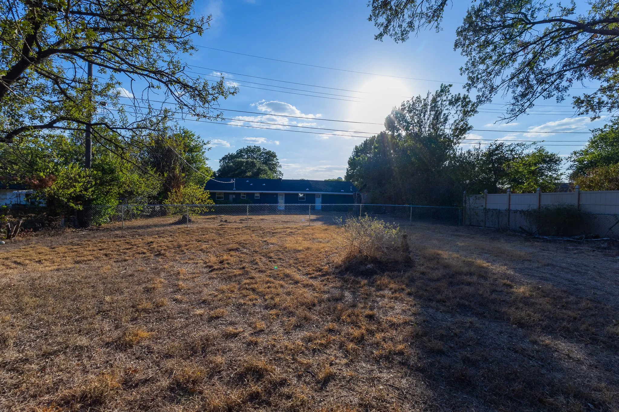 Expansive lot featuring mature trees and a chain-link fence