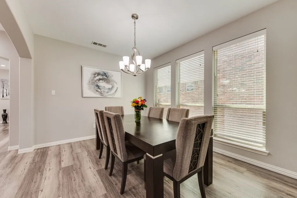 Dining area featuring wood-finish flooring, a contemporary chandelier, multiple windows with blinds, and light gray wall tones