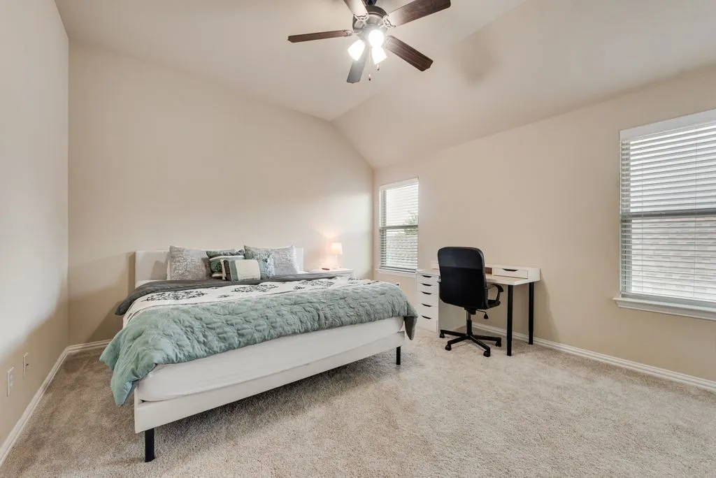 Vaulted ceiling with a ceiling fan, two windows, wall-to-wall carpeting, and neutral wall tones