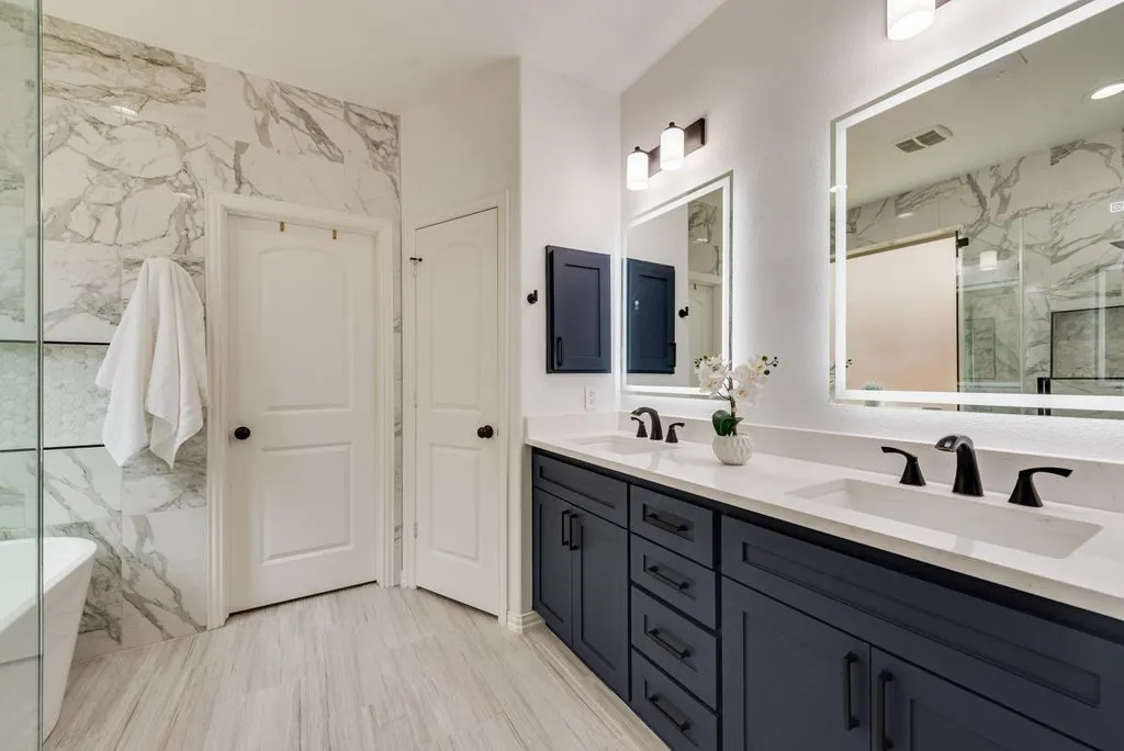 Double vanity with dark blue cabinetry, matte black fixtures, and illuminated mirrors