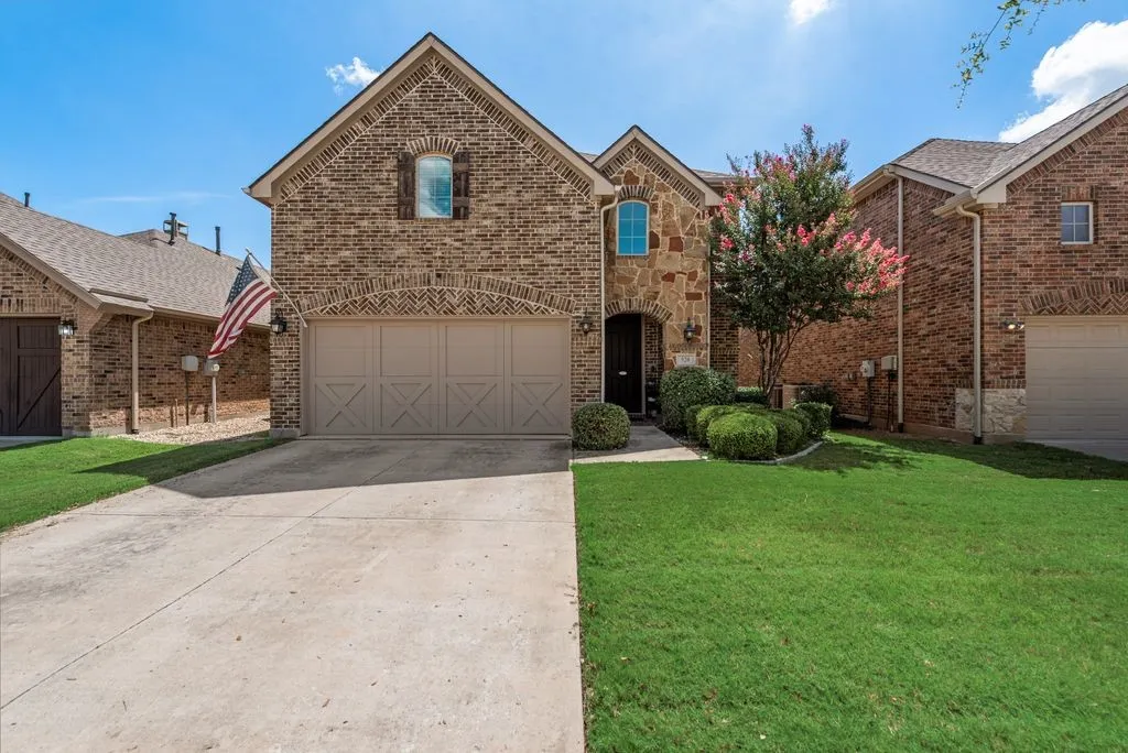 Brick and stone facade, arched entry, decorative garage door, concrete driveway, and established front landscaping