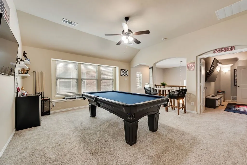 Carpeted recreation room featuring vaulted ceilings, a ceiling fan, and multiple windows with blinds