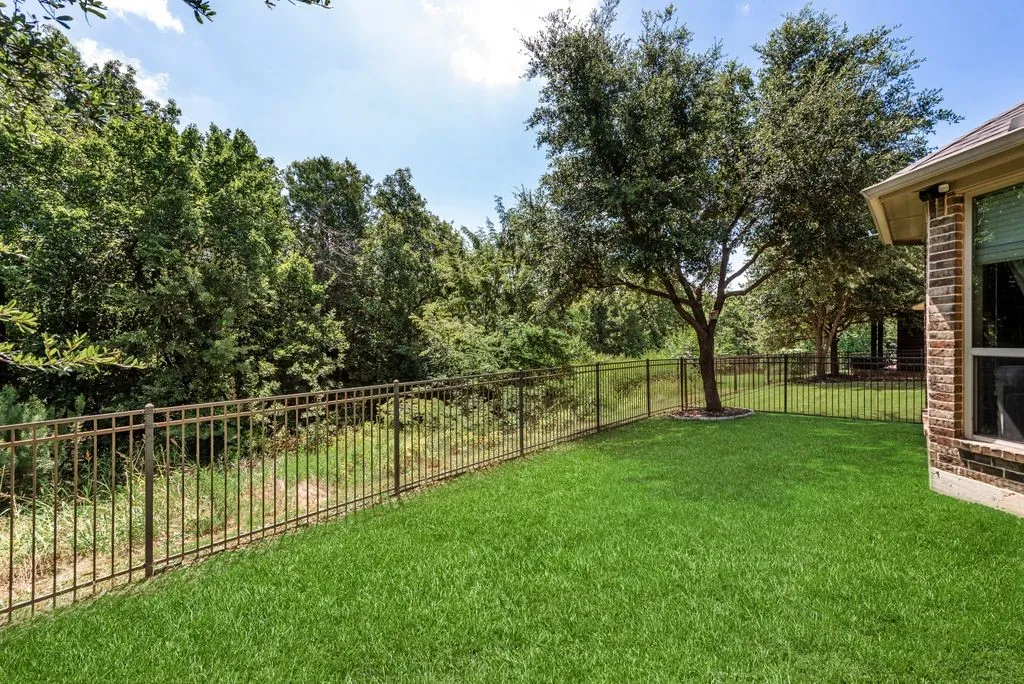 Expansive rear yard featuring a manicured lawn, established trees, and a durable metal fence