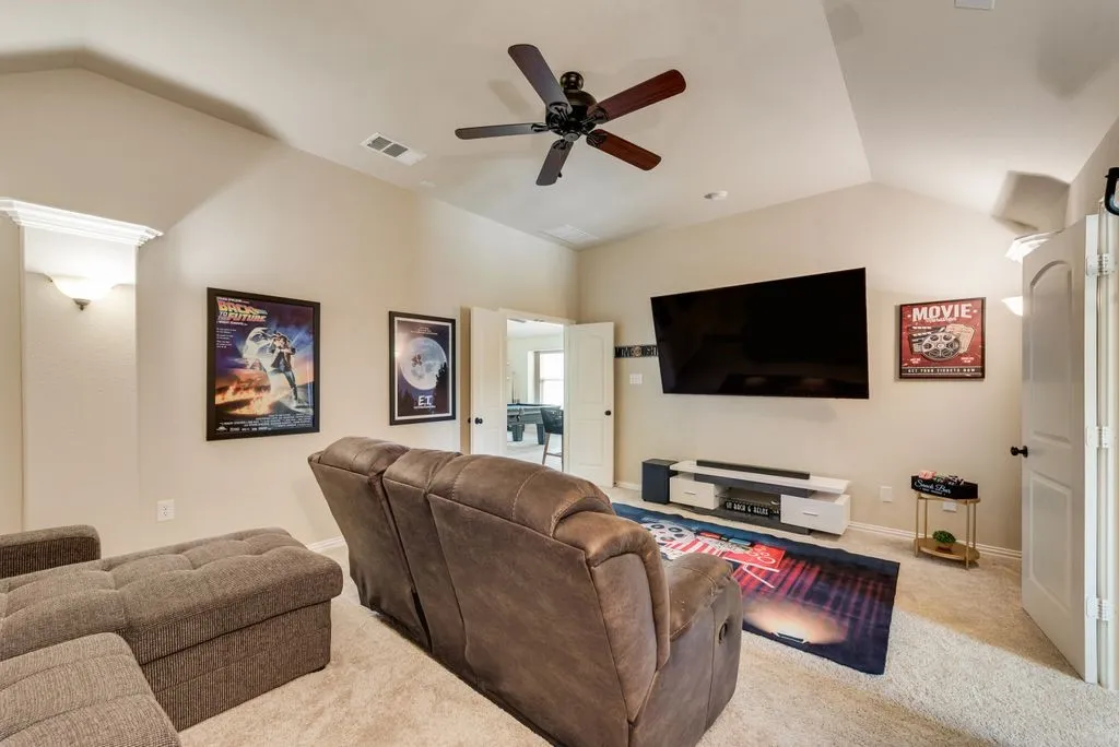 Vaulted ceiling with ceiling fan, wall-mounted television, and sconce lighting