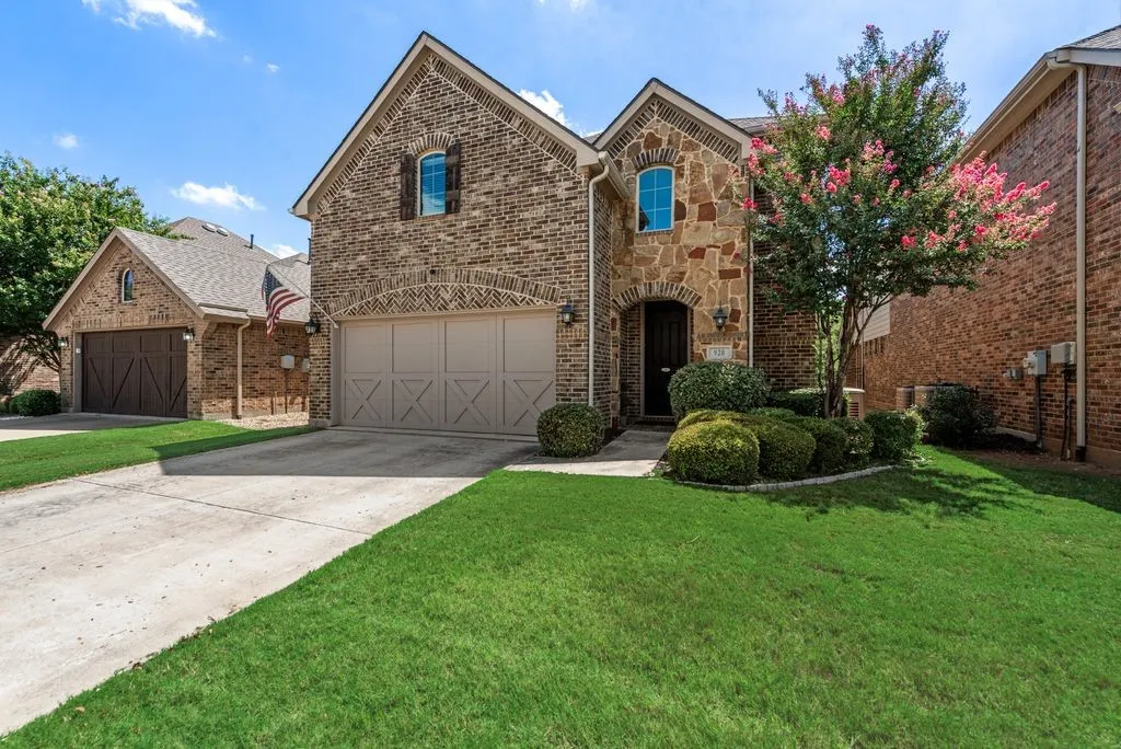 Brick and stone exterior with arched entryways, concrete driveway, attached garage, and established landscaping