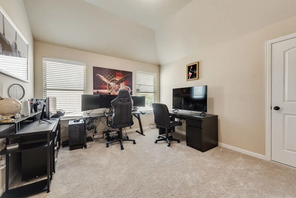 Vaulted ceiling, two windows with blinds, light-toned carpeting, white trim, and a white interior door with a black doorknob