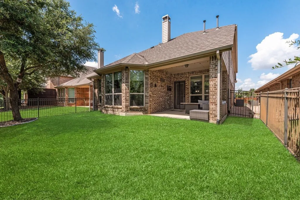 Expansive backyard featuring a lush lawn, mature tree, and a covered patio
