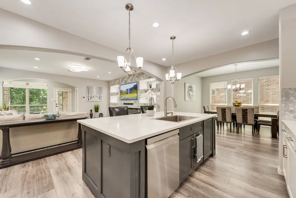 Kitchen island with white countertop and integrated sink, stainless steel dishwasher, wood-finish flooring, recessed lighting, and chandelier lighting