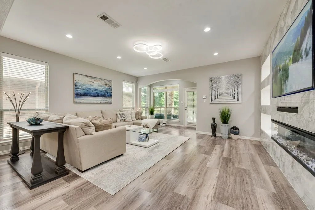 Recessed lighting, wood-finish flooring, accent wall with built-in fireplace, multiple windows, and a glass-paneled door