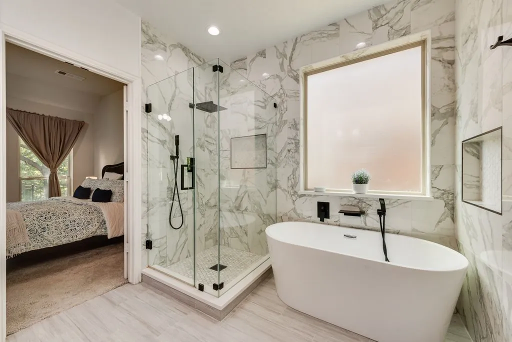 Freestanding soaking tub with matte black fixtures, glass-enclosed shower with a rainfall showerhead, and floor-to-ceiling tile