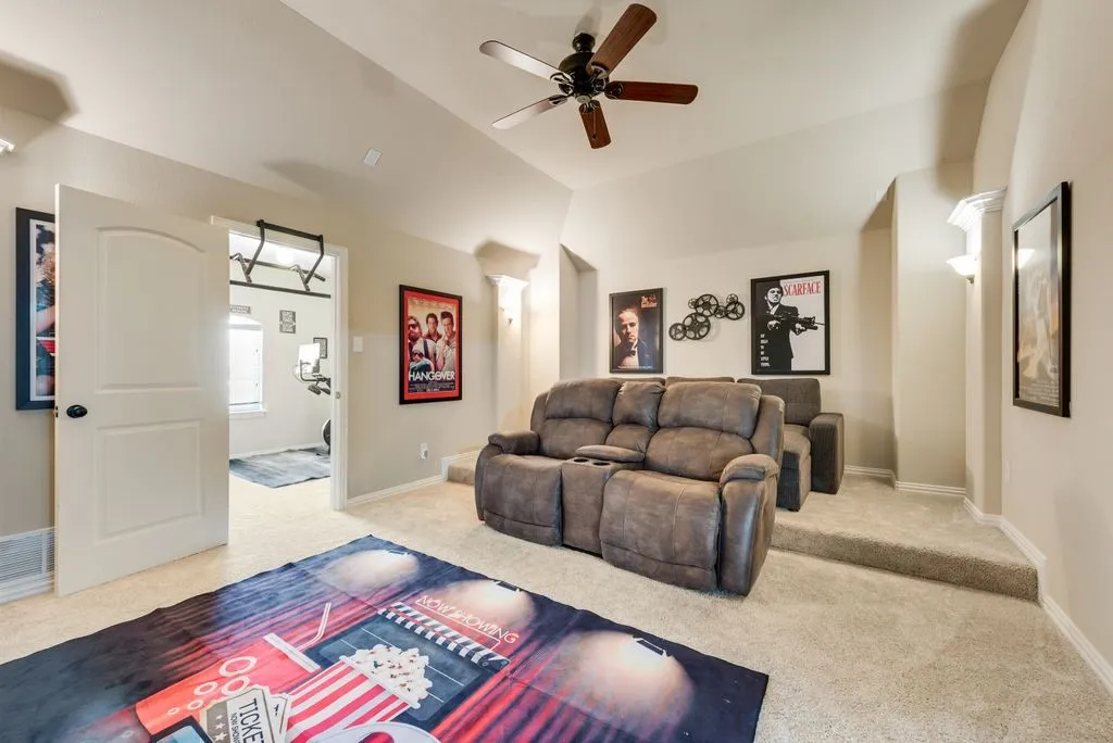 Carpeted entertainment space with a ceiling fan, wall sconces, and a tiered seating area