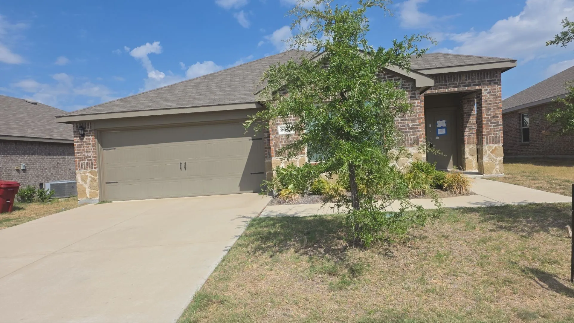 Brick exterior with stone accents, covered entry, attached garage, and concrete driveway