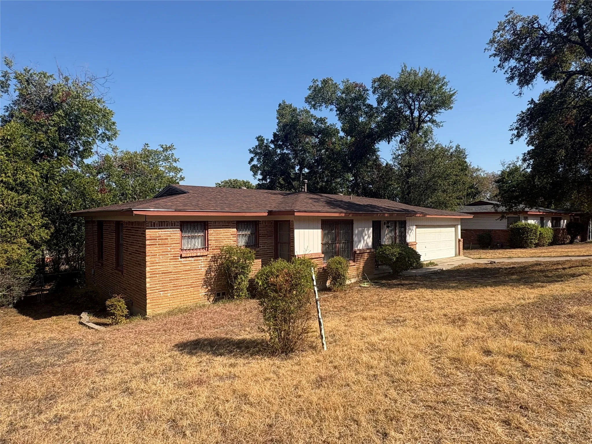 Brick exterior with a brown shingle roof, attached garage, and surrounding mature trees