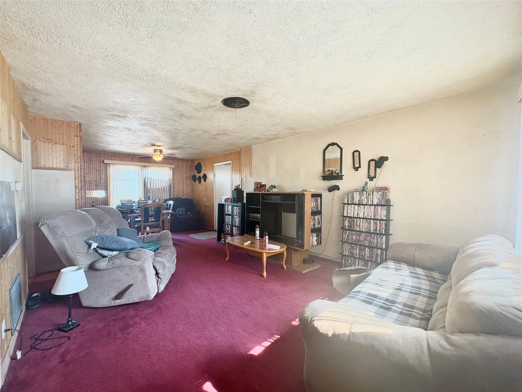 Carpeted living area with textured ceiling, wood paneling, and a ceiling-mounted light fixture