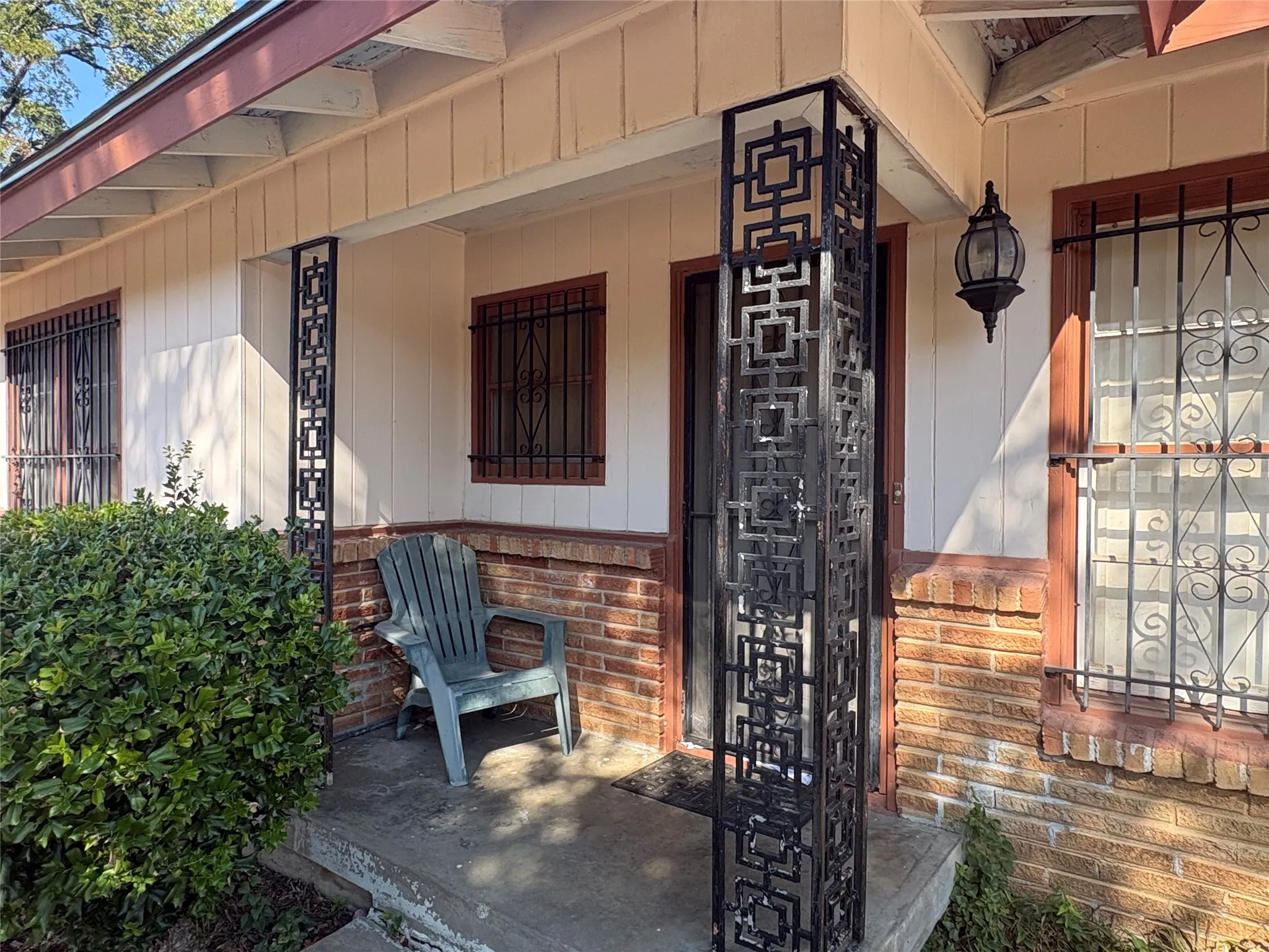 Covered porch with decorative metal columns, brick wainscoting, and an exterior wall light fixture