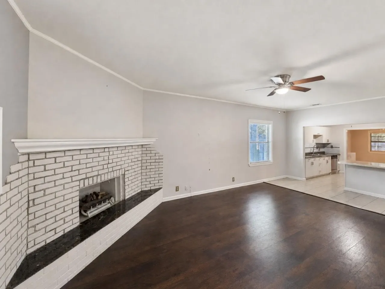 White brick fireplace with dark mantel, wood-finish flooring, ceiling fan, and crown molding