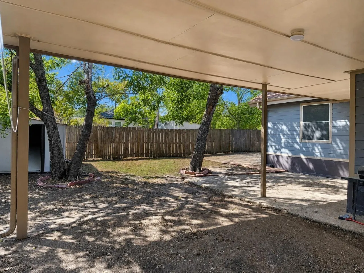 Covered patio extending to an outdoor area with a wood fence, mature trees, and a utility shed
