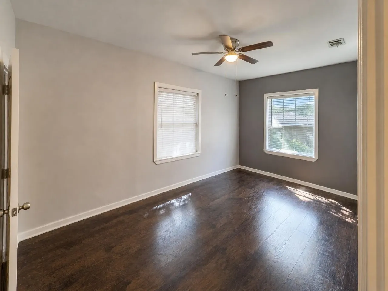 Wood-finish flooring, two windows with blinds, and a ceiling fan with light fixture