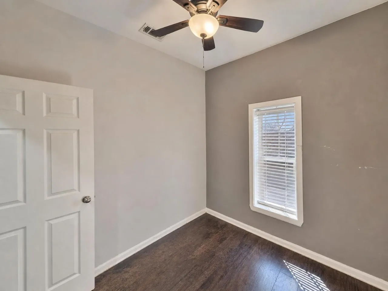 Wood-finish flooring, ceiling fan with light fixture, single window with blinds, and paneled interior door