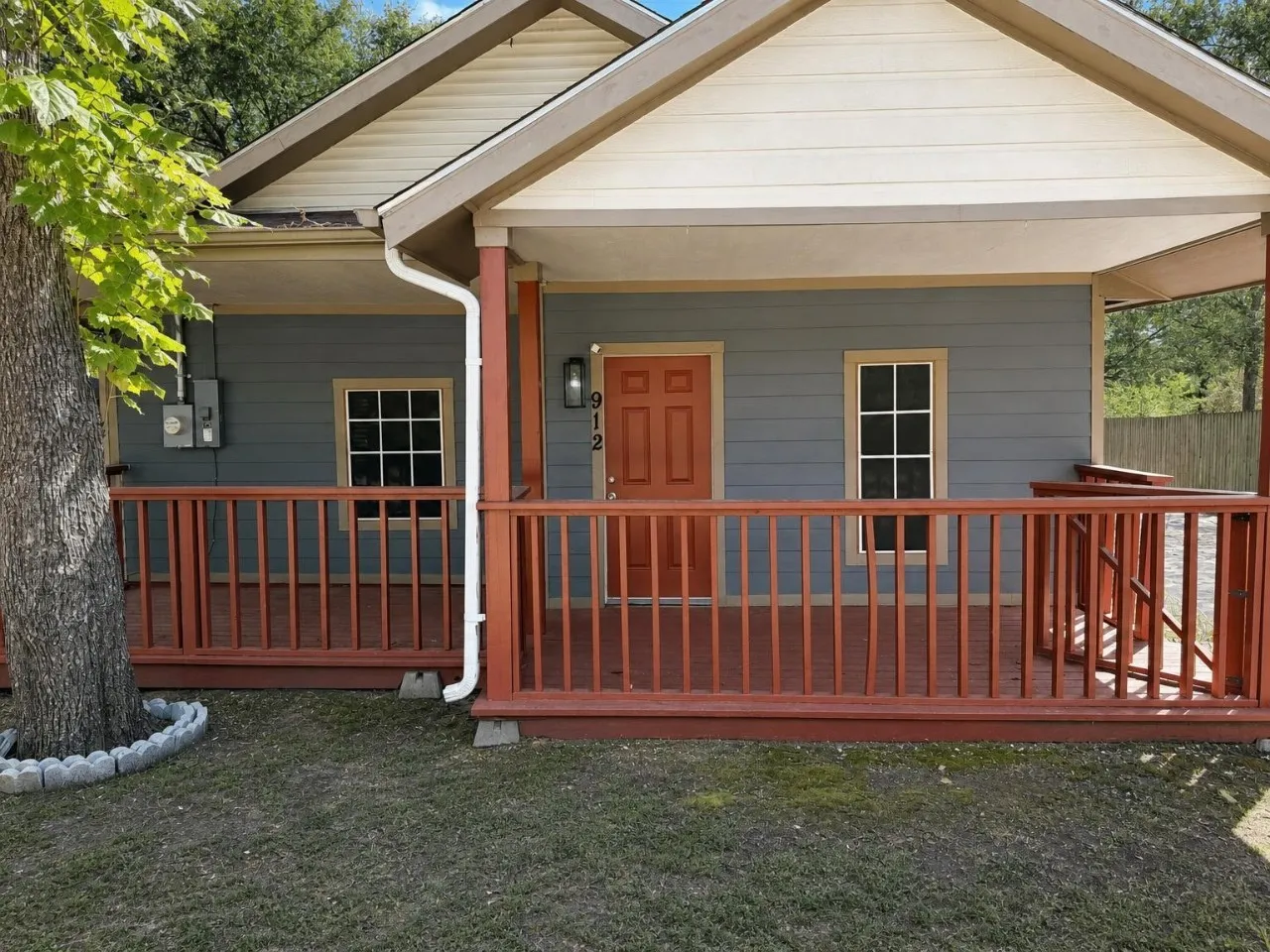 Covered front porch with wood railings and posts, light blue siding, and an orange entry door