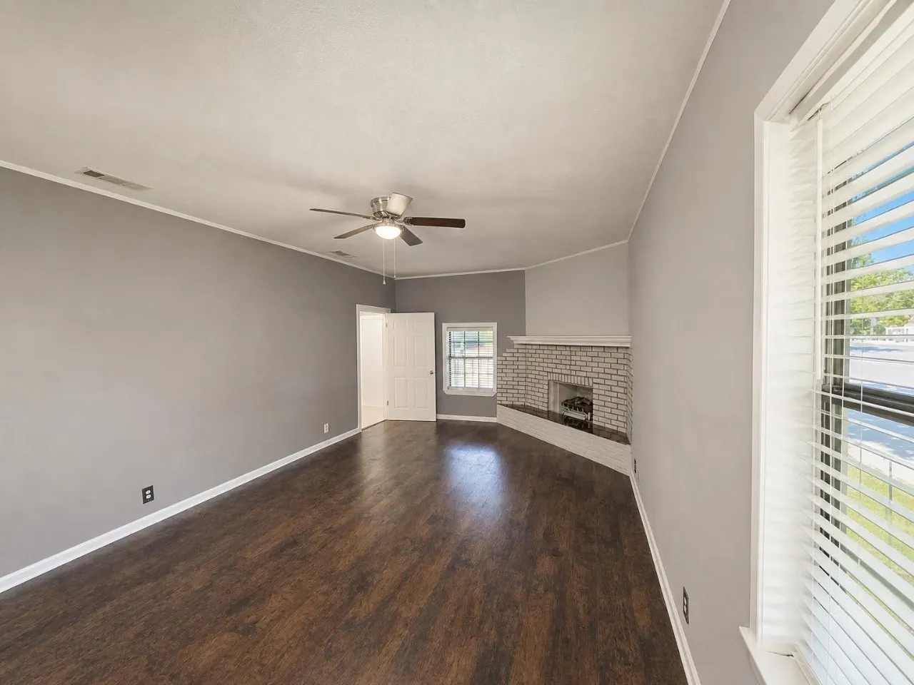 Spacious room featuring wood-finish flooring, a ceiling fan, and a painted brick fireplace