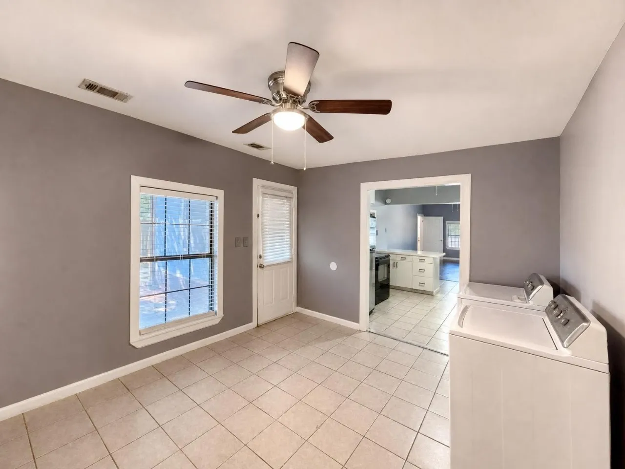 Tile flooring, ceiling fan with integrated lighting, white-framed window with blinds, white door with integrated blinds, and a neutral wall color