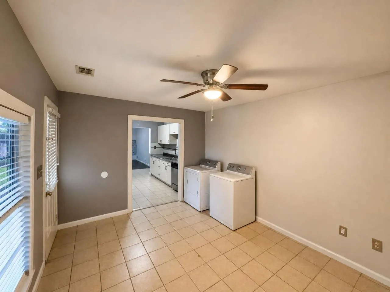 Neutral-toned tile flooring, ceiling fan with integrated lighting, and a white paneled door with integrated blinds