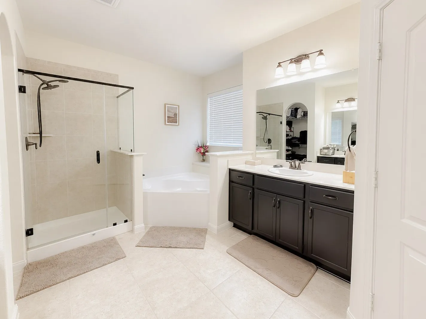 Spacious bathroom featuring a glass-enclosed shower, built-in bathtub, dual-sink vanity with dark wood cabinetry, a large wall-mounted mirror, and tiled flooring