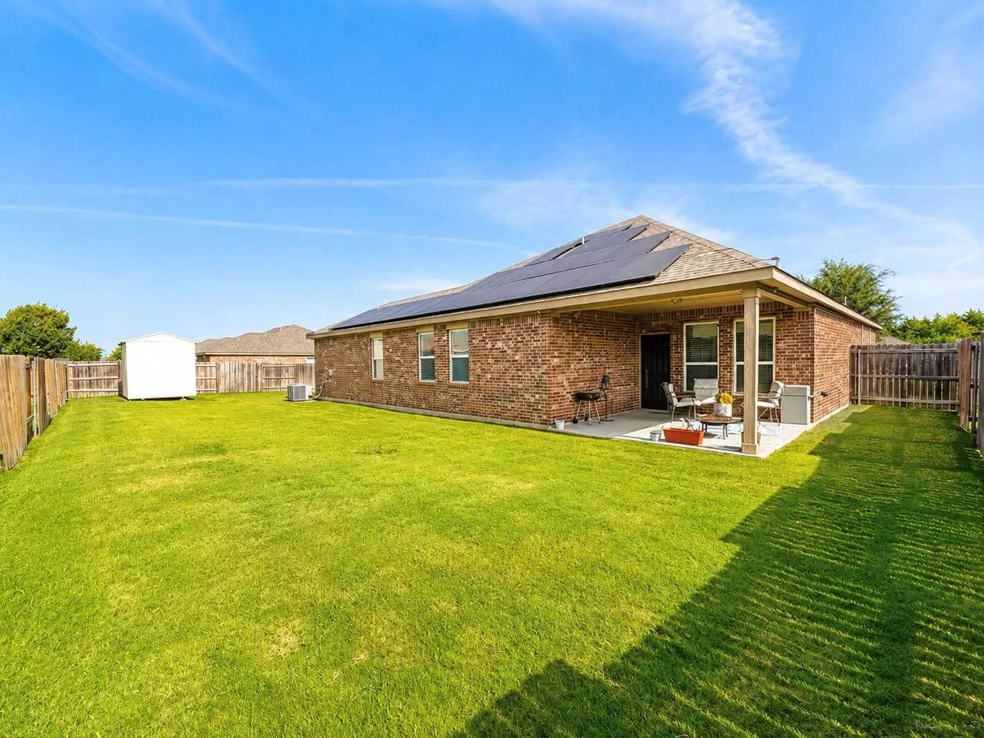 Expansive backyard featuring a manicured lawn, wood privacy fencing, and a dedicated storage shed