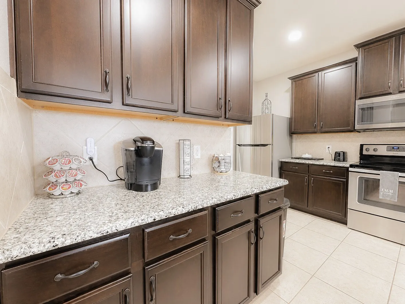 Dark wood-finish cabinetry, granite-style countertops, stainless steel appliances, ceramic tile backsplash, and ceramic tile flooring