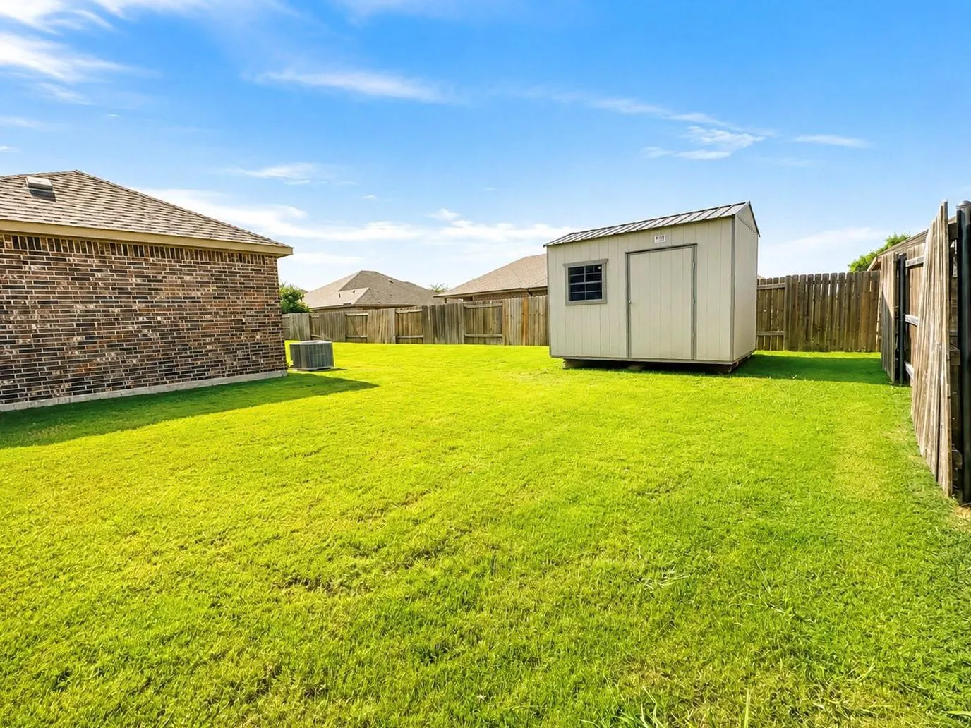 Expansive backyard featuring a manicured lawn, wood privacy fencing, and a dedicated storage shed