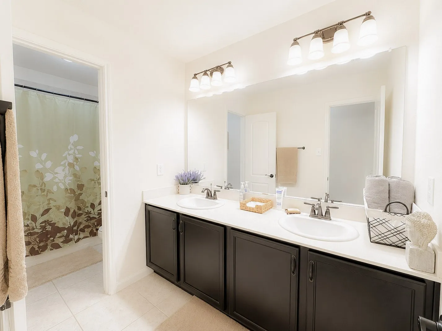 Dual sink vanity with dark wood-finish cabinetry, light-toned countertop, and full-width mirror