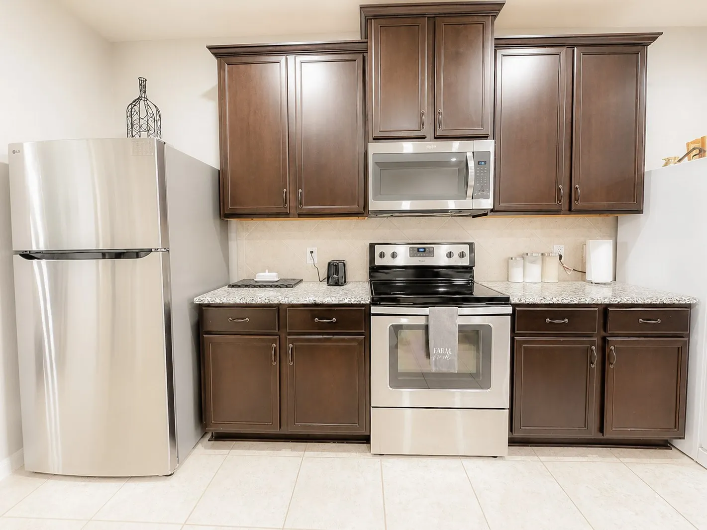 Kitchen featuring wood-finish cabinetry, granite-style countertops, stainless steel appliances, and a tiled floor