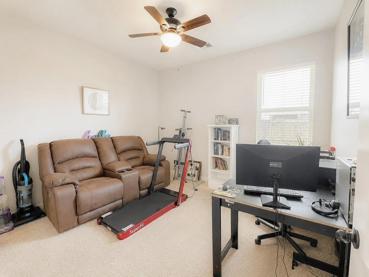 Neutral wall color, light-colored carpeting, window with blinds, ceiling fan with integrated lighting, and a built-in bookshelf