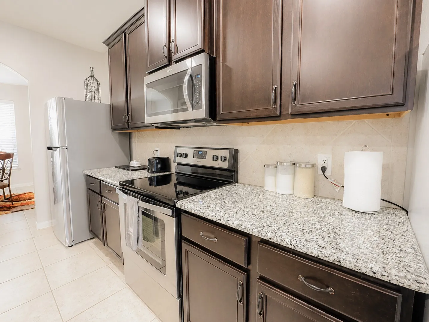 Dark wood-finish cabinetry, stainless steel microwave, stainless steel electric range, speckled countertops, and tile backsplash