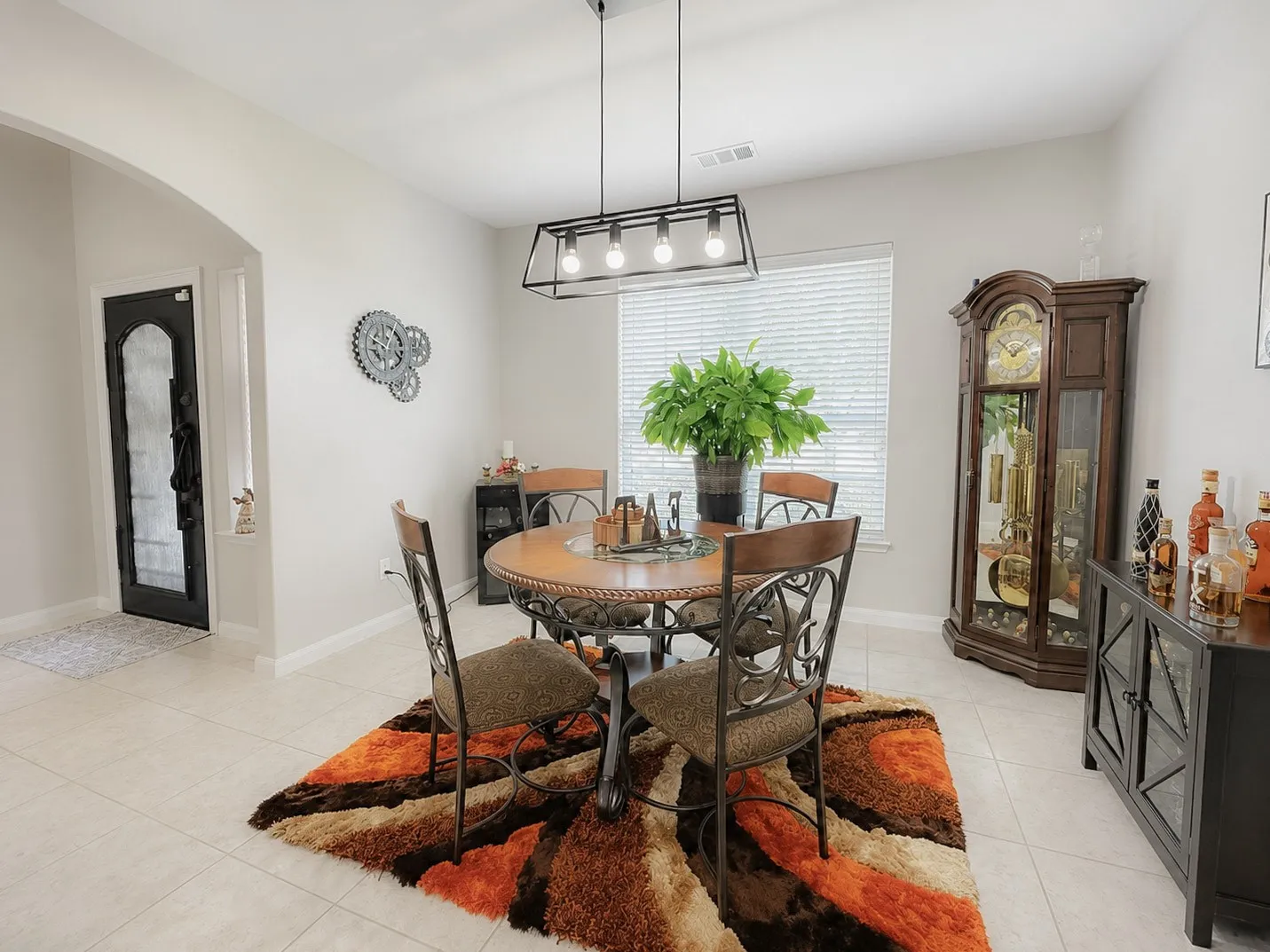 Recessed ceiling with a contemporary linear chandelier, arched doorway, tiled flooring, and a large window with blinds
