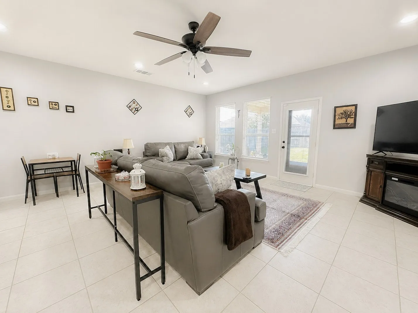 Recessed lighting throughout, ceiling fan with wood-finish blades, light-toned tile flooring, multiple windows, and a glass-paneled door