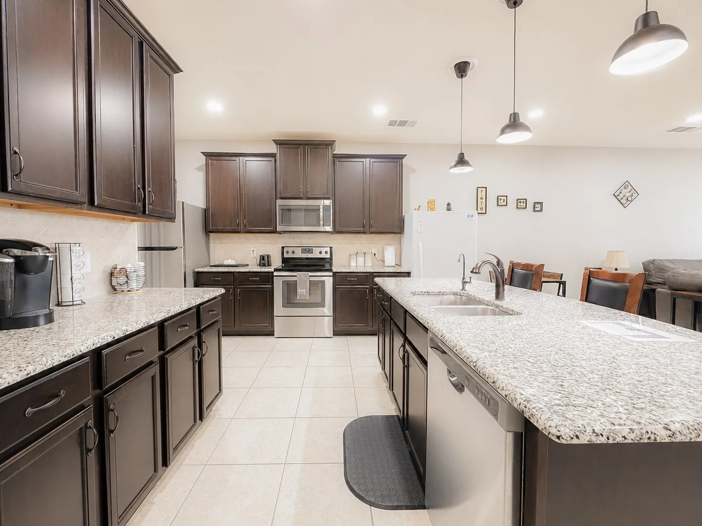 Kitchen featuring dark wood-finish cabinetry, light speckled countertops, stainless steel appliances, a double basin sink, and pendant lighting