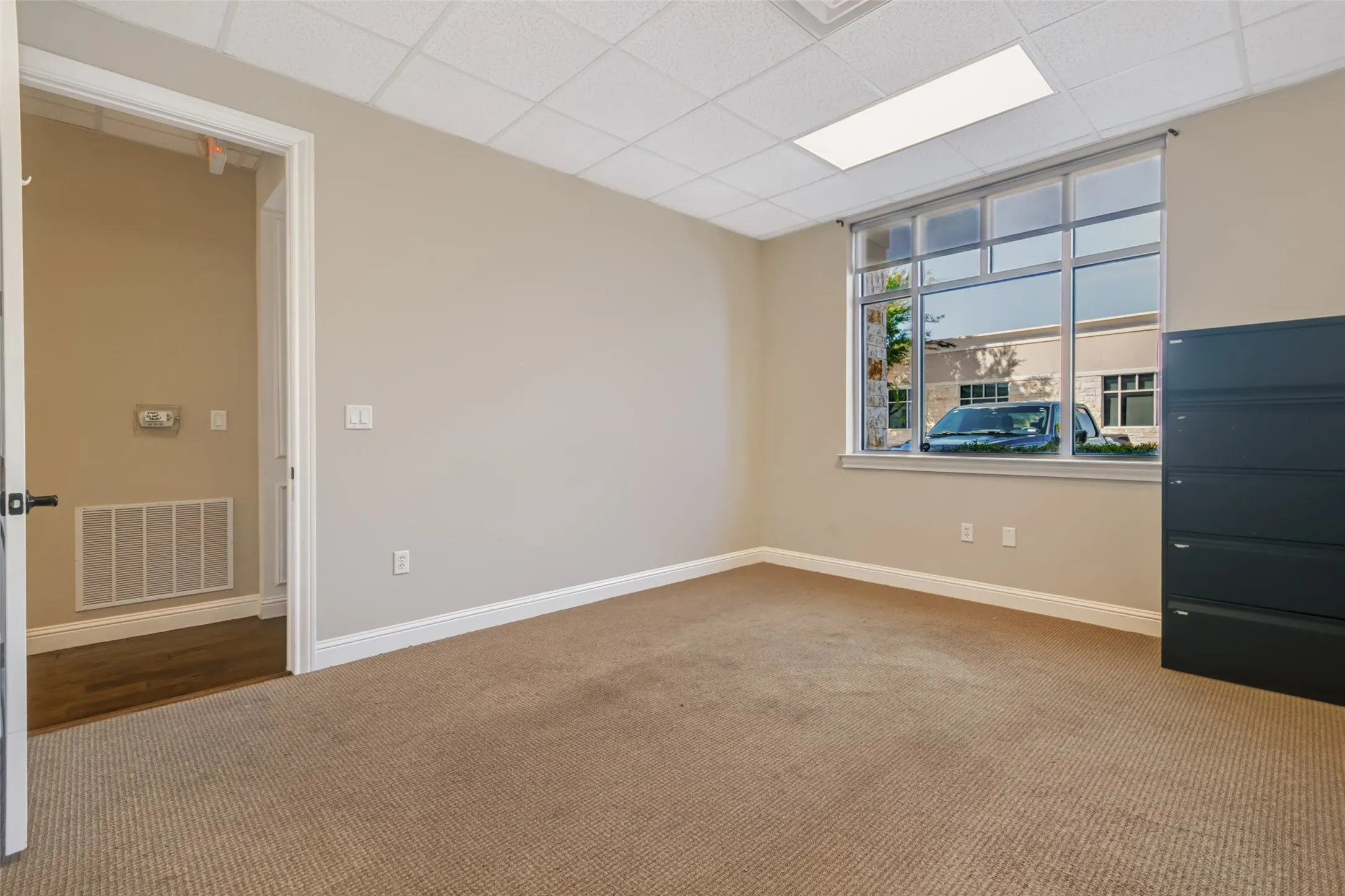 Carpeted room with a drop ceiling, transom window, and a white trim package