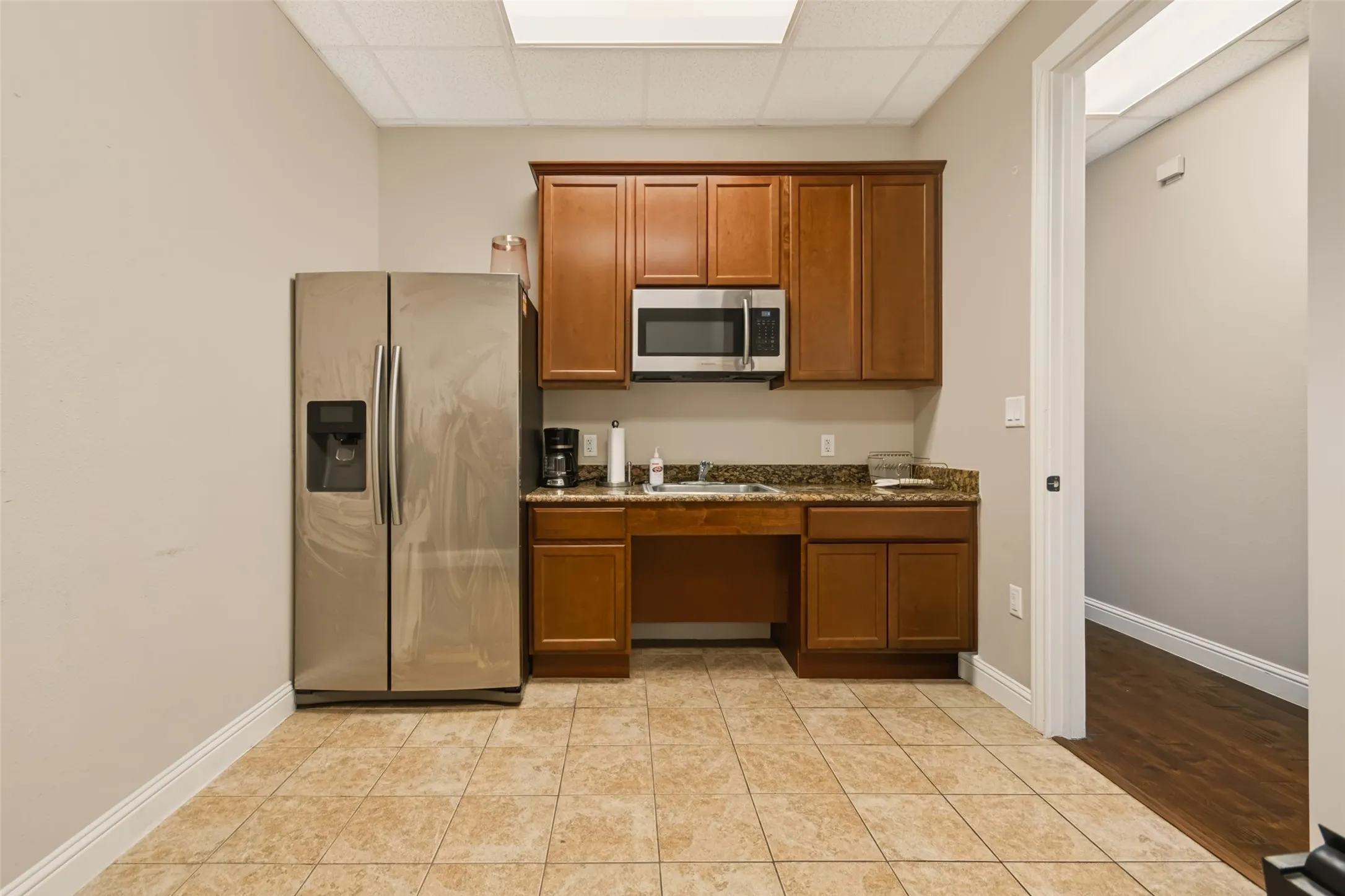 Kitchenette featuring wood cabinetry, stainless steel microwave, stone-finish countertops, and tile flooring
