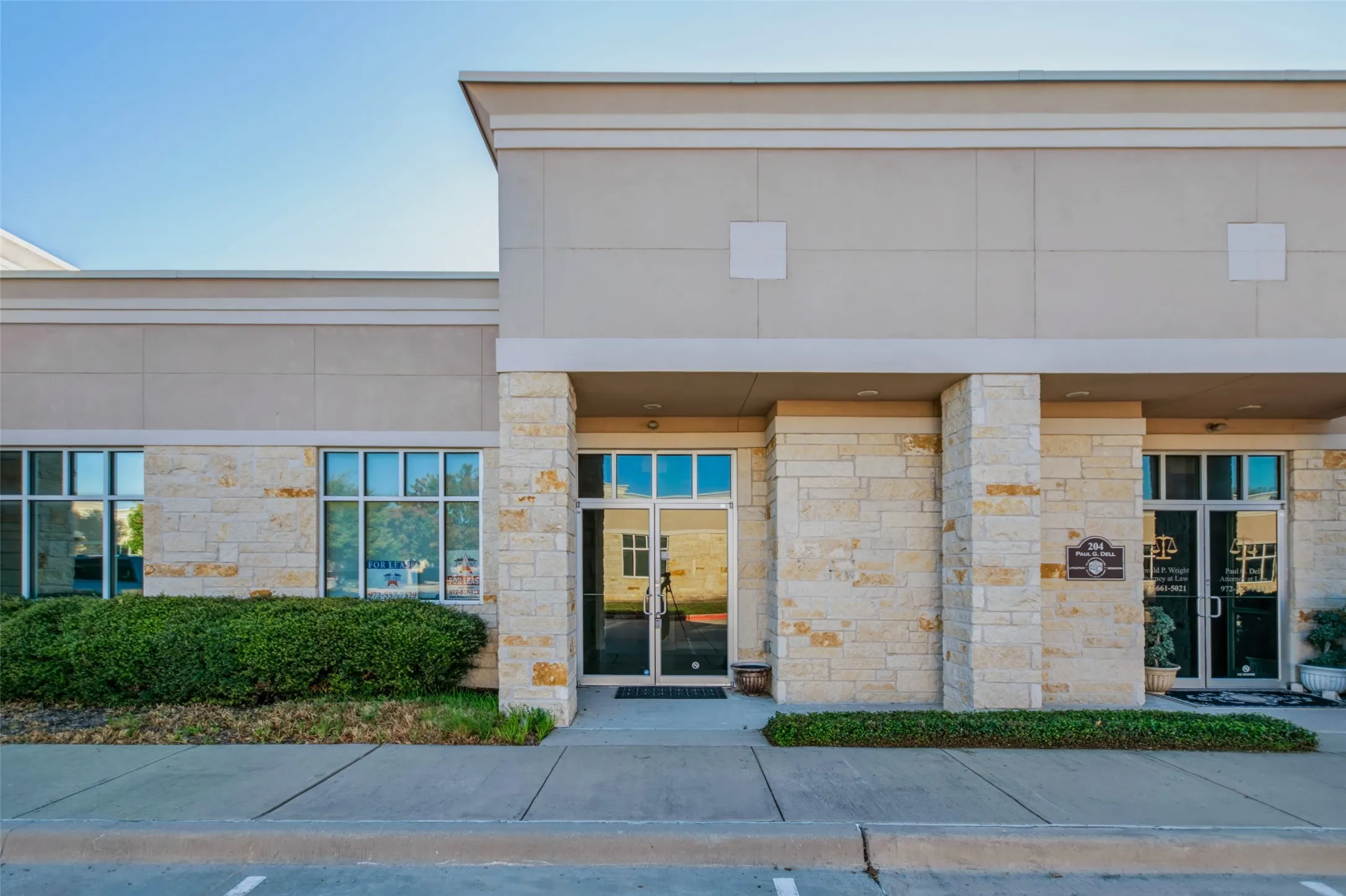 Stone facade with a neutral stucco finish, large commercial windows, and double glass entry doors