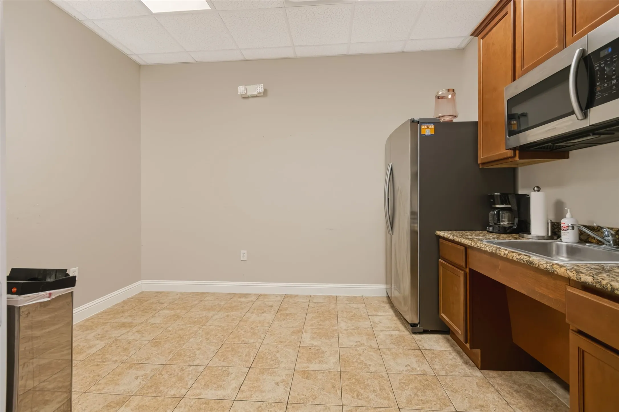 Kitchenette featuring tile flooring, wood-finish cabinetry, stainless steel appliances, and a solid surface countertop with an integrated sink